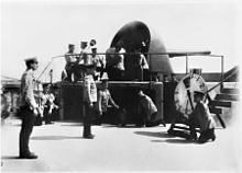 A large gun encassed in an open backed metal turret atop a fort