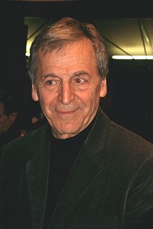 Photograph of the head and shoulders of a man who is looking somewhat to the left of the camera. He has a slightly quizzical smile. He is wearing a dark green sports coat and a pullover shirt.